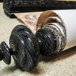 Handcrafted black wooden finial securing a rolled vintage canvas world map. Decorative scroll rod highlights rustic craftsmanship and antique-inspired wall décor for offices, libraries, and studies.
