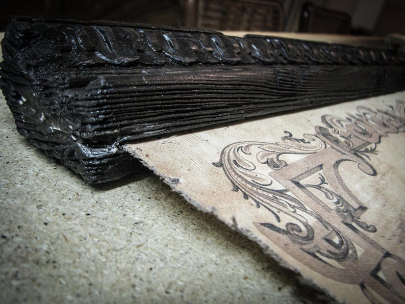 Macro view of a handcrafted Victorian-style wooden map hanger with carved detailing and black stained finish beside premium canvas. Artisan scroll frame for vintage world map wall art and classic home décor.