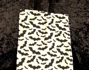 May include: A white tote bag with black bat silhouettes printed all over. The bag has black fabric handles.