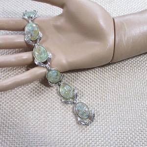 May include: A silver-tone link bracelet featuring five oval-shaped cabochons in a pale, mottled green and yellow hue. Each cabochon is set within a polished metal frame, connected by decorative silver-colored links that create a continuous chain.