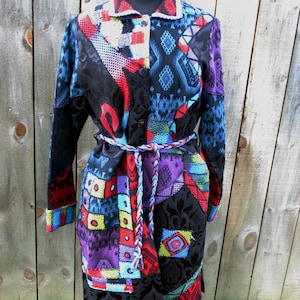 May include: A long, button-down coat with a patchwork design. The coat features a variety of colors and patterns, including red, blue, purple, and black. It has a matching belt and is displayed on a mannequin.