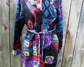 May include: A long, button-down coat with a patchwork design. The coat features a variety of colors and patterns, including red, blue, purple, and black. It has a matching belt and is displayed on a mannequin.
