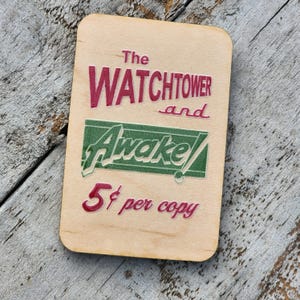 May include: A vintage wooden sign advertising "The Watchtower and Awake!" for 5 cents per copy. The sign is printed in red and green on a light brown background.