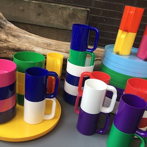 以下が含まれることがあります： カラフルな積み重ね可能なプラスチックカップのセット。カップは異なる色のバンドで飾られています。カップは黄色いトレイと青と緑のトレイに配置されています。カップはパーティー、ピクニック、または日常の使用に最適です。