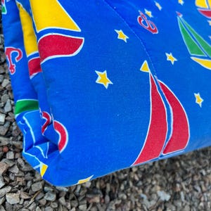 May include: A blue quilted fabric with a pattern of red, yellow, and green sailboats and stars. The fabric is folded in half and the edge is visible.