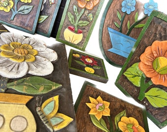 Könnte beinhalten: Eine Sammlung von Wandkunst aus Holz mit geschnitzten Blumen und Schmetterlingen. Die Stücke sind in leuchtenden Farben bemalt, darunter Gelb, Blau, Rot, Grün und Orange. Die Blumen sind stilisiert und haben einen verspielten Charakter.