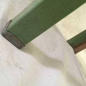 K&ouml;nnte beinhalten: Nahaufnahme eines gr&uuml;nen Metalltischbeins mit einem grauen Metallfu&szlig;. Das Bein ist in einem matten Gr&uuml;nton lackiert und hat eine leicht strukturierte Oberfl&auml;che.