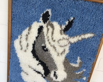 Könnte beinhalten: Ein gerahmter Teppich mit blauem Hintergrund und einem weißen, grauen und schwarzen Einhorn-Design.