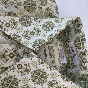 Puede incluir: Una camisa blanca con un patrón geométrico verde y dorado. La camisa tiene una etiqueta que dice "Ely & Walker Tall Man" y "100% algodón Hecho en EE. UU.".