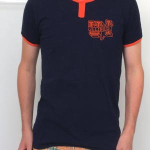 Könnte beinhalten: Ein marineblaues T-Shirt mit orangefarbenem Besatz und einer Vintage-Grafik mit der Aufschrift "U of Illinois".
