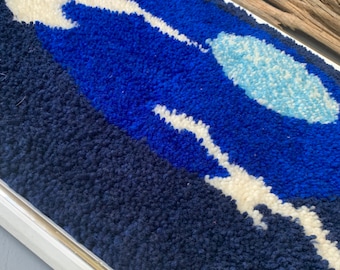 Könnte beinhalten: Ein gerahmtes Wandbild mit einem abstrakten Design in Blau, Weiß und Hellblau. Das Design besteht aus geschlungenem Garn und erinnert an eine Landschaft.