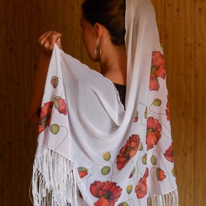 Puede incluir: Chal blanco con borde de flecos y dise&ntilde;o de flores de amapola. El chal est&aacute; hecho de una tela ligera y tiene un tacto delicado.