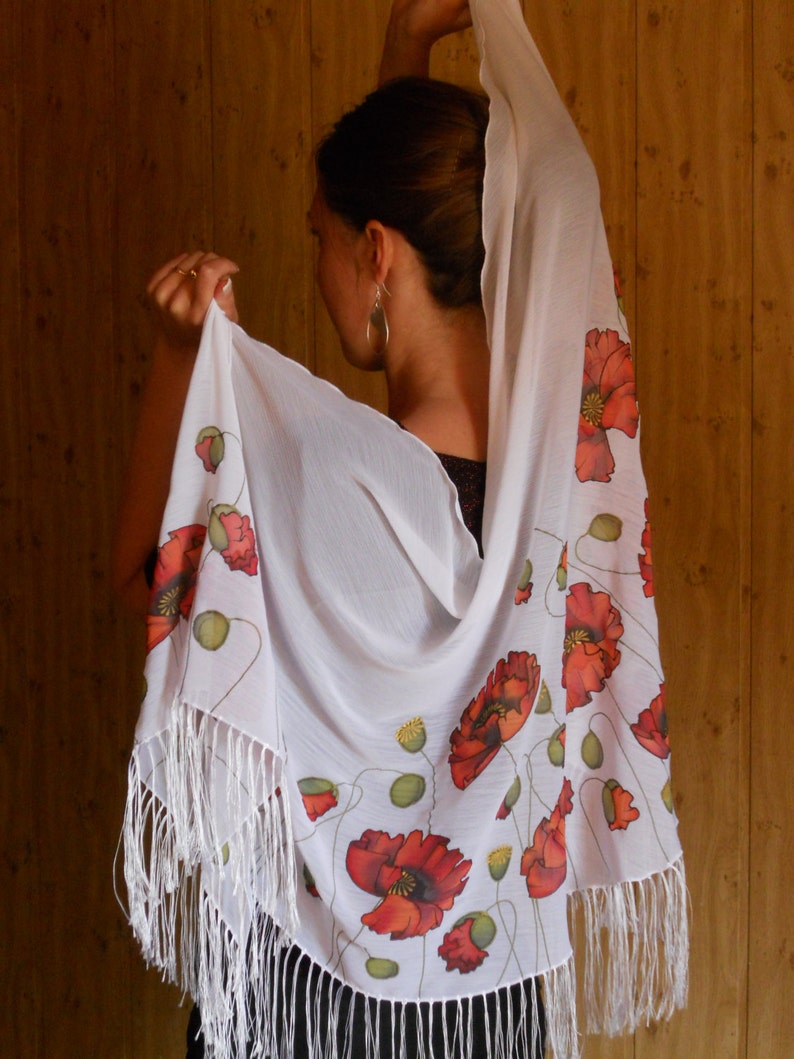 Puede incluir: Chal blanco con borde de flecos y dise&ntilde;o de flores de amapola. El chal est&aacute; hecho de una tela ligera y tiene un tacto delicado.