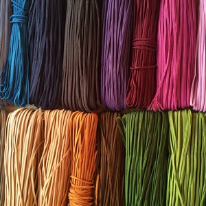 May include: Assortment of colourful elastic cords in various shades of blue, purple, brown, red, pink, green, and orange. The cords are arranged in rows and are all the same length.