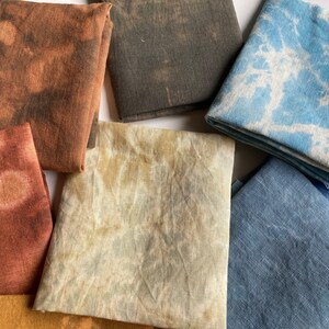 Op de afbeelding: Een verzameling van acht stoffen vierkanten in verschillende tinten bruin, blauw en beige. De stoffen vierkanten hebben een tie-dye effect en zijn in een willekeurig patroon gerangschikt.