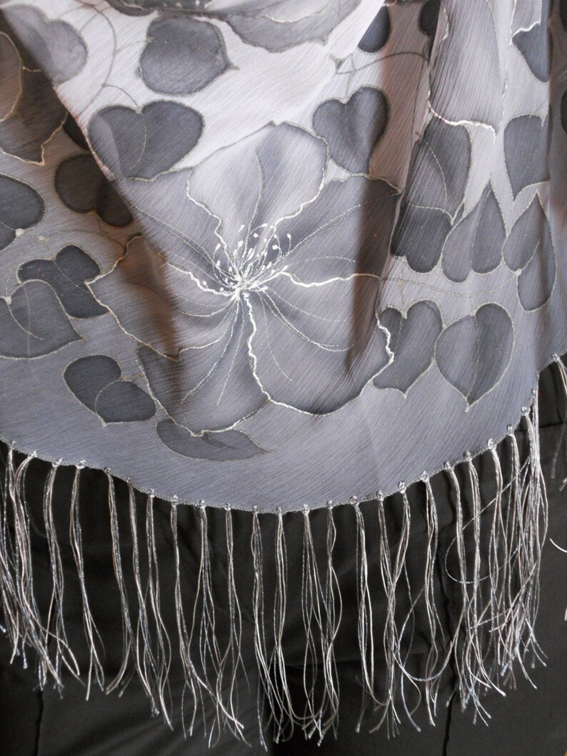 Puede incluir: Una bufanda de seda gris con un dise&ntilde;o floral y un borde de flecos. La bufanda est&aacute; hecha de una tela ligera y tiene una sensaci&oacute;n delicada.