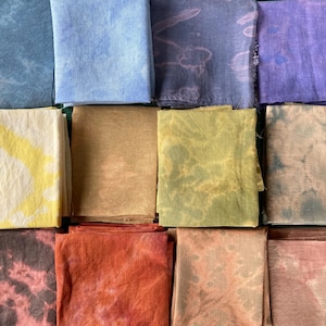 Op de afbeelding: Een verzameling van 12 stoffen vierkanten in verschillende tinten blauw, geel, bruin, rood en paars. De stoffen vierkanten zijn allemaal tie-dye geverfd met verschillende patronen.