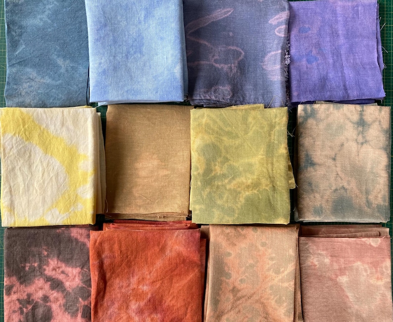 Op de afbeelding: Een verzameling van 12 stoffen vierkanten in verschillende tinten blauw, geel, bruin, rood en paars. De stoffen vierkanten zijn allemaal tie-dye geverfd met verschillende patronen.