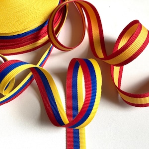 Könnte beinhalten: Gerolltes gelb, rot und blau gestreiftes Band. Das Band ist auf einer weißen Oberfläche gekräuselt und angeordnet. Die Farben sind lebendig und das Band scheint aus einem gewebten Material zu bestehen. Das Band wird wahrscheinlich zum Basteln oder Dekorieren verwendet.