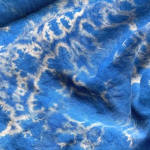 May include: Blue fabric with a white tie-dye pattern. The fabric is wrinkled and has a soft, textured appearance.