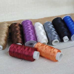 Puede incluir: Surtido de carretes de hilo en varios colores, incluyendo beige, marr&oacute;n, morado, blanco, gris, negro, azul, rojo y naranja.
