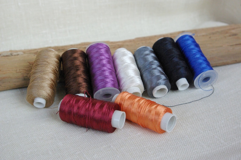 Puede incluir: Surtido de carretes de hilo en varios colores, incluyendo beige, marr&oacute;n, morado, blanco, gris, negro, azul, rojo y naranja.