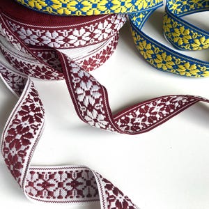 Op de afbeelding: Close-up van decoratieve linten in verschillende kleuren. Eén spoel is bordeauxrood met witte bloempatronen. Een andere is geel en blauw met bloempatronen. De linten worden waarschijnlijk gebruikt voor knutselen of versieringen.