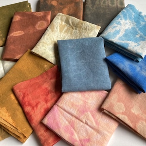 Op de afbeelding: Een verzameling van 12 stoffen vierkanten in verschillende tinten bruin, blauw, roze en rood. De stoffen vierkanten zijn allemaal van verschillende grootte en hebben een tie-dye patroon.