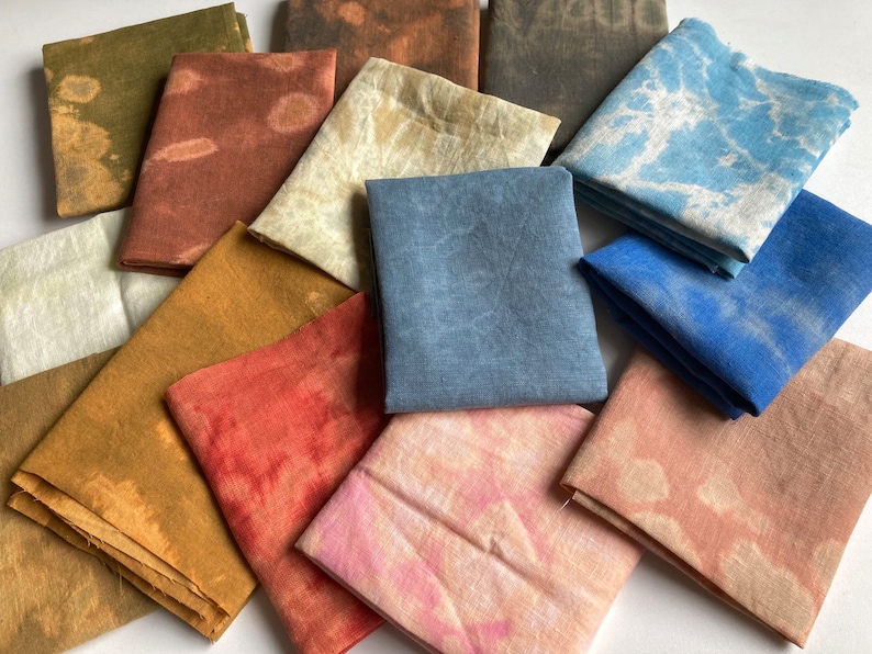 Op de afbeelding: Een verzameling van 12 stoffen vierkanten in verschillende tinten bruin, blauw, roze en rood. De stoffen vierkanten zijn allemaal van verschillende grootte en hebben een tie-dye patroon.