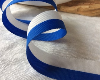 May include: A white ribbon with a blue stripe running along the edge. The ribbon is curled and twisted.