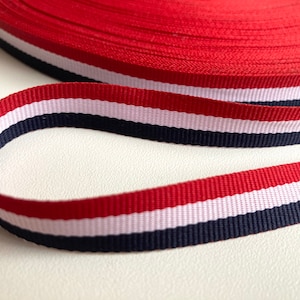 May include: Red, white, and navy blue striped ribbon. The ribbon is woven with a textured pattern.