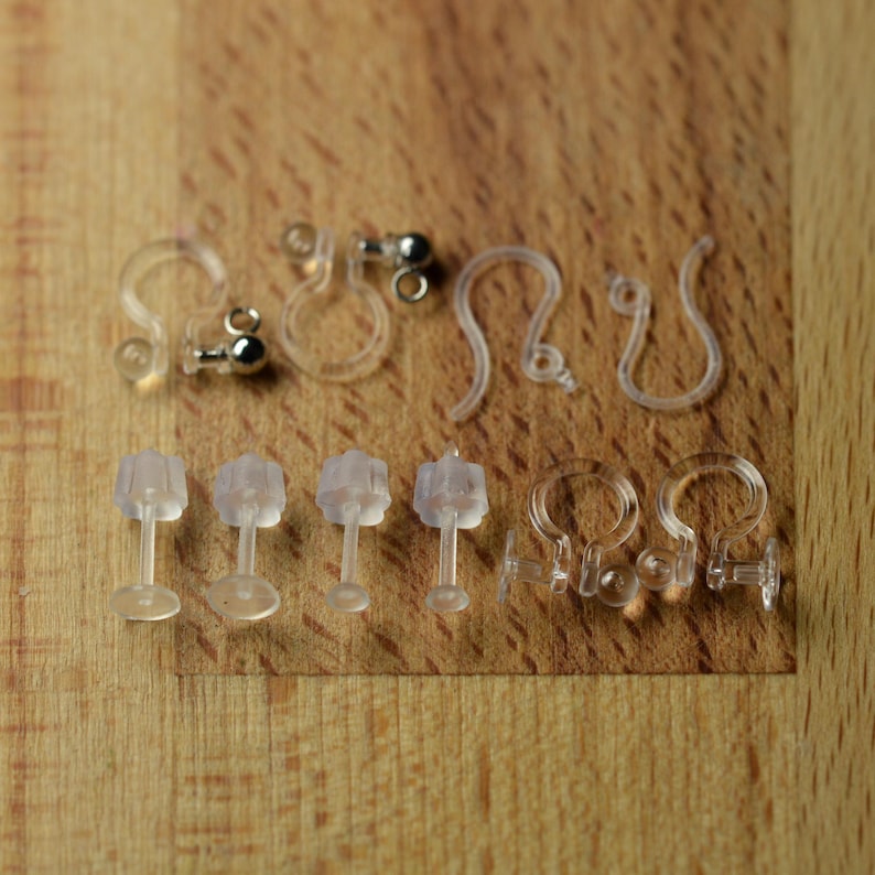 May include: A collection of clear plastic earring components including clip-on findings with small silver-toned metal balls, U-shaped hook findings, and straight post backs with flat circular bases, all designed for jewelry making and assembly.