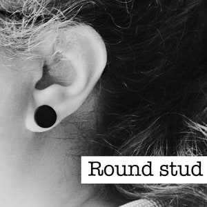 Puede incluir: Un pendiente de bot&oacute;n redondo negro es visible en la oreja de una persona. La imagen es en blanco y negro, con el texto "Round stud" en un rect&aacute;ngulo blanco.