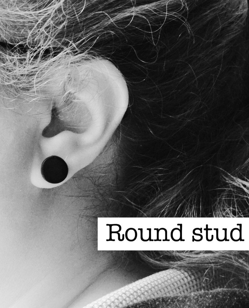 Puede incluir: Un pendiente de bot&oacute;n redondo negro es visible en la oreja de una persona. La imagen es en blanco y negro, con el texto "Round stud" en un rect&aacute;ngulo blanco.