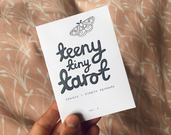 May include: A black and white illustration of a moth on a white card with the text "teeny tiny tarot theory + simple spreads vol. 1" printed on it.