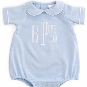 May include: A light blue baby romper with a Peter Pan collar and short sleeves. The romper has white piping around the collar and sleeves. The letters "RPE" are embroidered in white on the front.