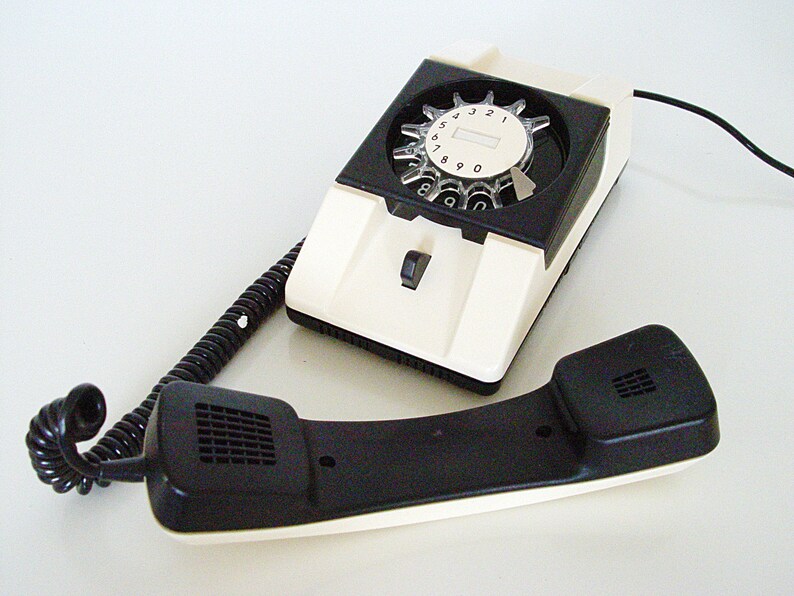 Puede incluir: Un tel&eacute;fono de disco blanco con un disco negro y un auricular negro. El tel&eacute;fono tiene un cable blanco.