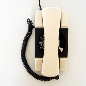 Puede incluir: Un tel&eacute;fono de disco vintage con un auricular blanco y una base negra. El tel&eacute;fono tiene un cable negro en espiral.