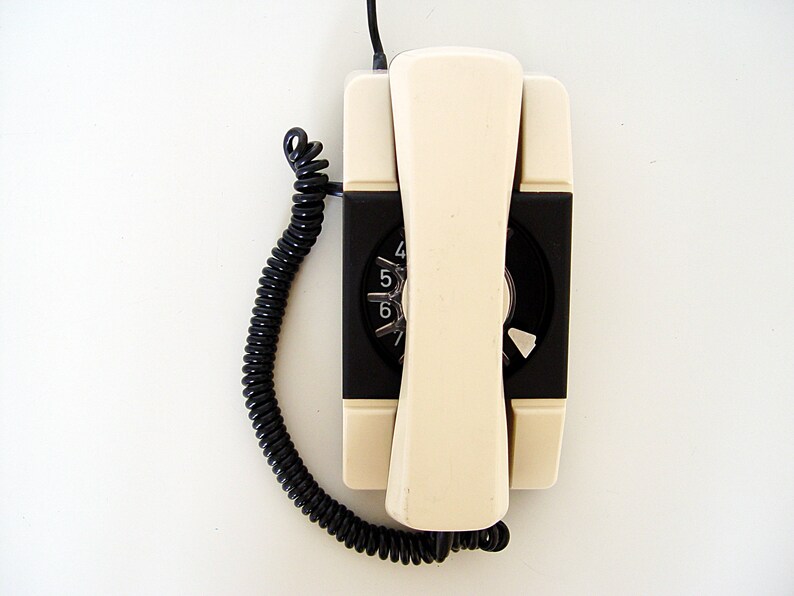 Puede incluir: Un tel&eacute;fono de disco vintage con un auricular blanco y una base negra. El tel&eacute;fono tiene un cable negro en espiral.