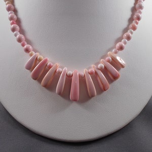 May include: A pink shell necklace with a graduated design. The necklace is made of small round beads and larger, teardrop-shaped shells.