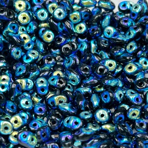 May include: A close-up shot of a pile of iridescent blue and black beads. The beads have a unique shape with two holes, and they reflect light with a shimmering effect. These beads are ideal for jewelry making and crafting.