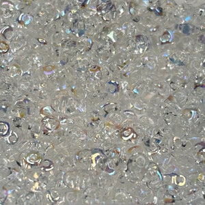 May include: A close-up of iridescent clear glass beads. The beads are small and round, with a slightly irregular shape. They have a shimmering, rainbow-like effect.