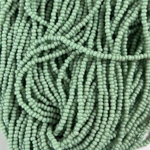 May include: Close-up of a pile of small, round, light green beads. The beads are strung together, creating a textured surface. The beads are uniform in size and shape, and the color is consistent throughout.