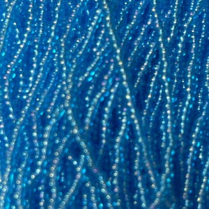 May include: Close-up of a vibrant blue yarn, densely packed with a shimmering, iridescent quality. The yarn strands are interwoven, creating a textured surface with a sparkling effect. The color is a deep, saturated blue.