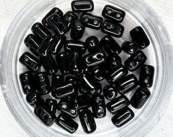 May include: A close-up of a container filled with black rectangular beads. The beads have two holes in each.