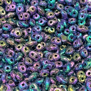 May include: A close-up of a pile of iridescent purple and green seed beads. The beads are small and have a teardrop shape with two holes.