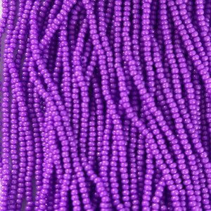 May include: A close-up shot of numerous small, round, purple beads. The beads are strung together, forming a textured pattern. The vibrant purple beads are well-lit, showcasing the details of each individual bead. The beads are likely for crafting.