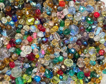 May include: A large assortment of colorful glass beads in various shapes and sizes. The beads are a mix of clear, opaque, and iridescent colors, including red, blue, green, gold, and silver.