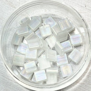 May include: A container of iridescent white square glass beads. The beads have a subtle shimmer and are perfect for jewelry making.