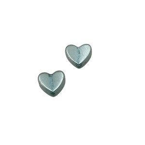 May include: Two small, silver-colored heart-shaped objects. The hearts are solid and have a slightly rounded, three-dimensional appearance. They are set against a plain white background.
